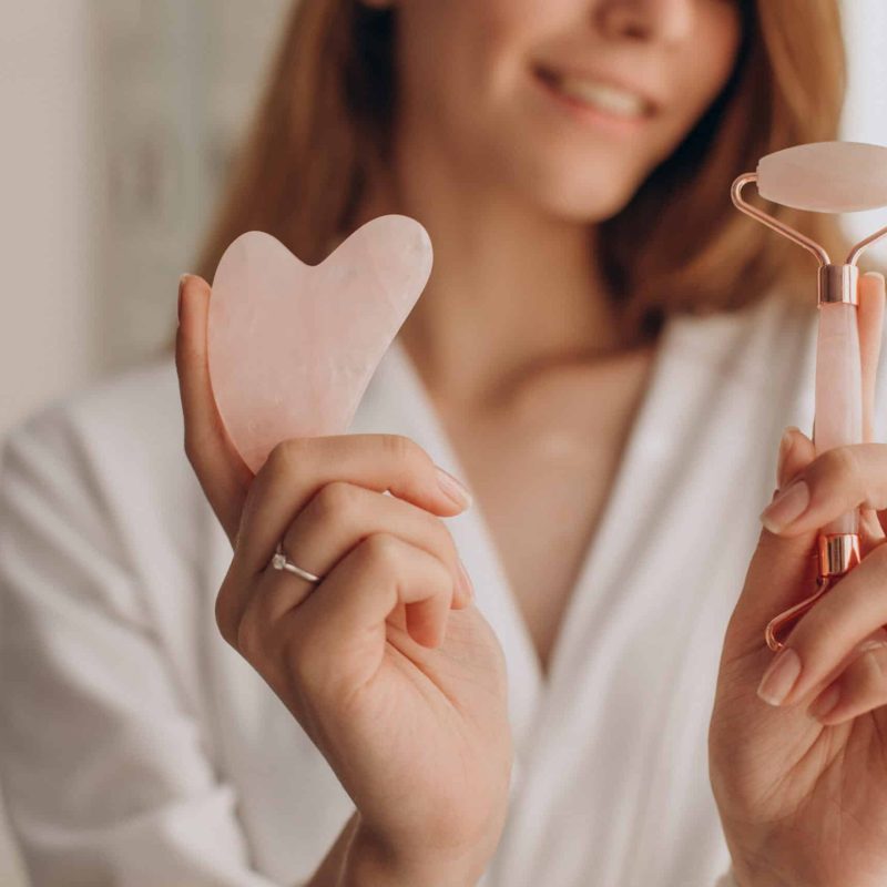 Woman making massage with gua sha stone and face roller